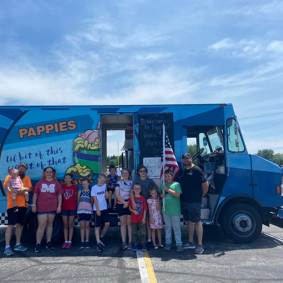 A group of adults and children pose in front of the blue Pappies Smokehouse & Lunch Box food truck.