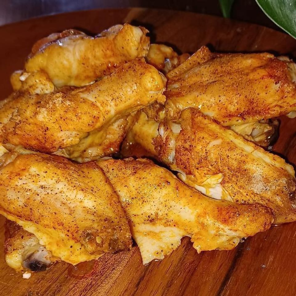 Close-up of golden-brown, seasoned chicken wings on a wooden platter, ready to be served.