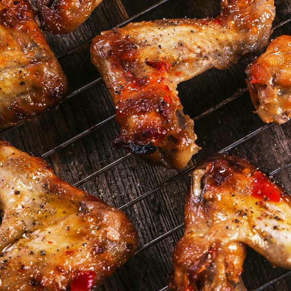 Close-up of several grilled chicken wings with a glossy sauce and black pepper on a grate.
