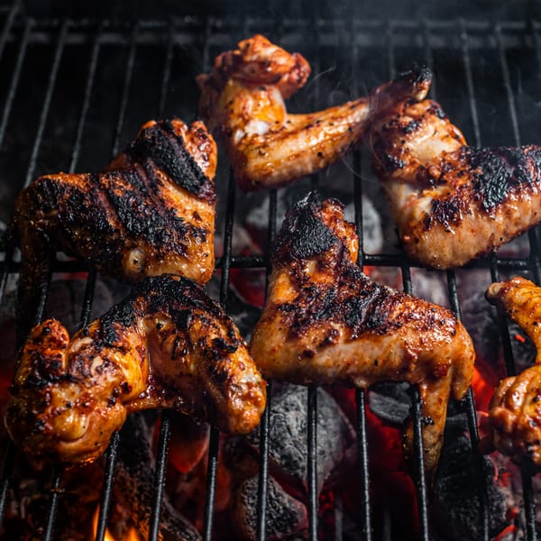 Pappies Smokehouse & Lunch Box BBQ chicken wings grilling over hot coals with smoke.