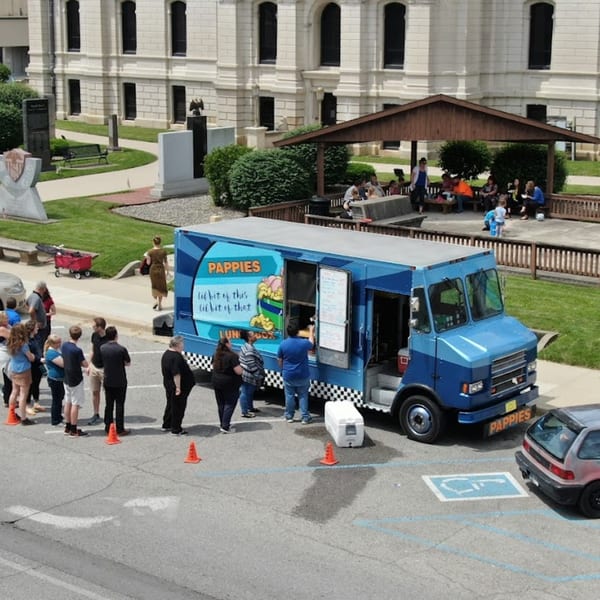 Pappies Smokehouse & Lunch Box food truck serving customers in a parking lot with a building in the background.