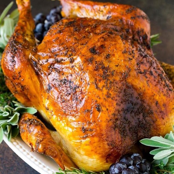 A whole roasted chicken, golden brown and seasoned, garnished with fresh herbs and dark berries.