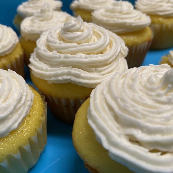A close-up of several yellow cupcakes with white swirled frosting on a blue surface.